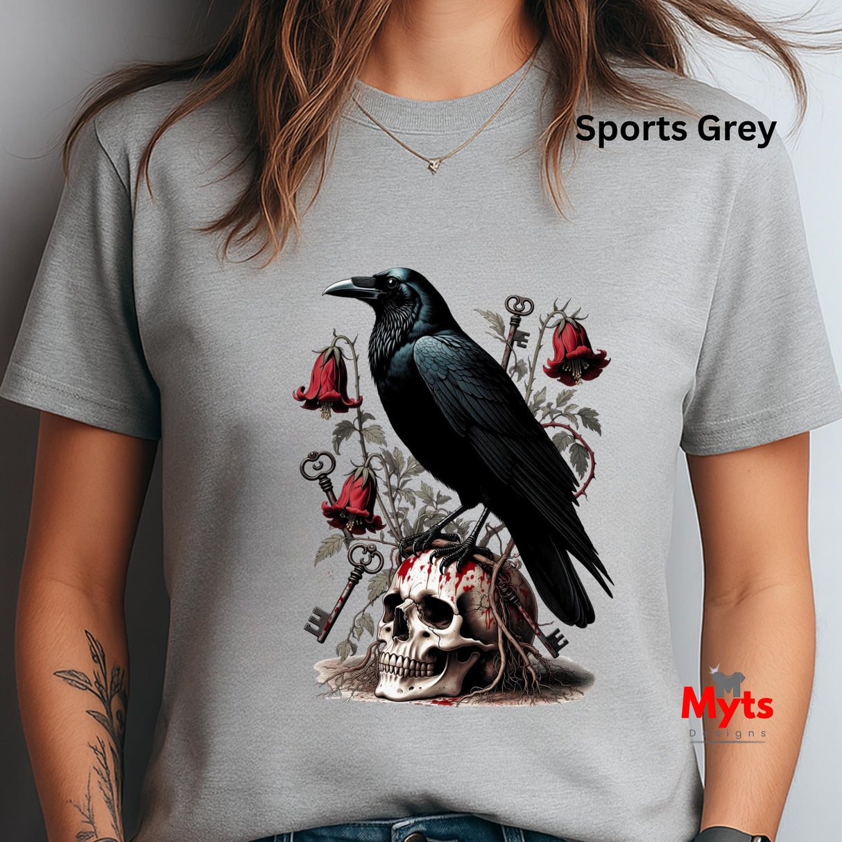 A woman wearing a light gray crewneck t-shirt with a gothic graphic print of a black raven perched on a skull, surrounded by red roses, keys, and bells. The text 'Sports Grey' is visible on the upper right, and a 'Myts' watermark is visible on the lower right.