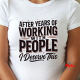 A white short-sleeve crewneck t-shirt with a humorous graphic that reads 'AFTER YEARS OF WORKING WITH PEOPLE I DESERVE THIS' in black and brown lettering. The t-shirt is shown on a model, with the model's arms and torso visible.
