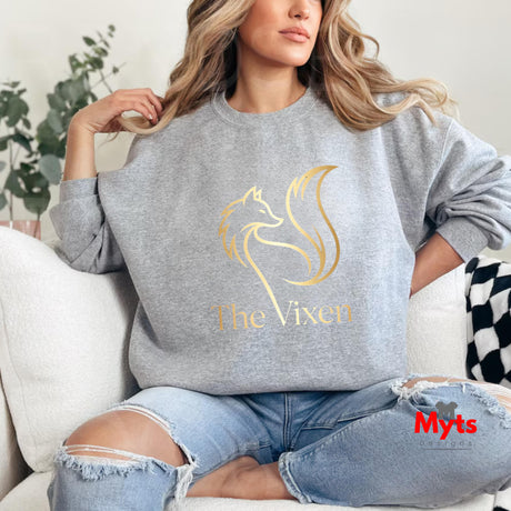 Person wearing a gray sweatshirt with a gold horse logo and 'The Vixen' text, sitting on a couch.