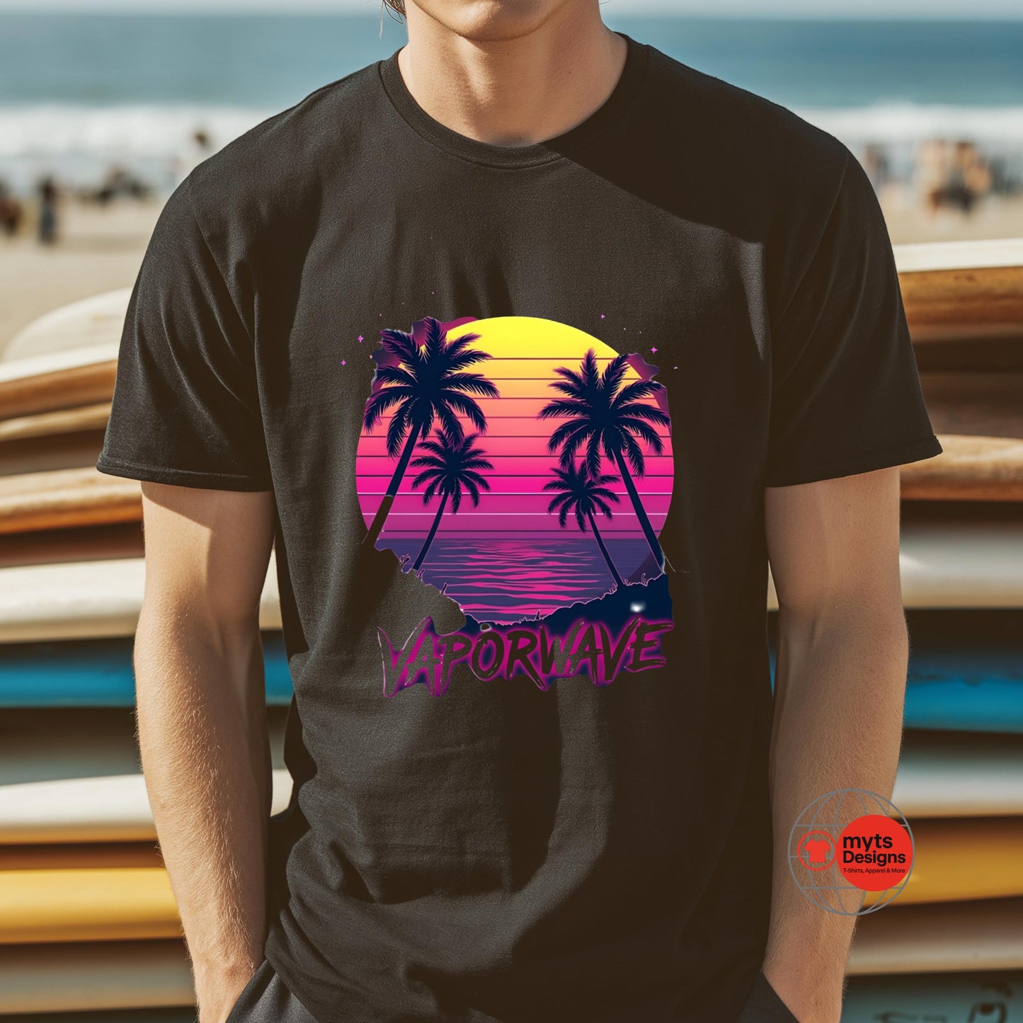 Person wearing a black t-shirt with a retro-themed design of palm trees and a sunset, standing in front of a beach.