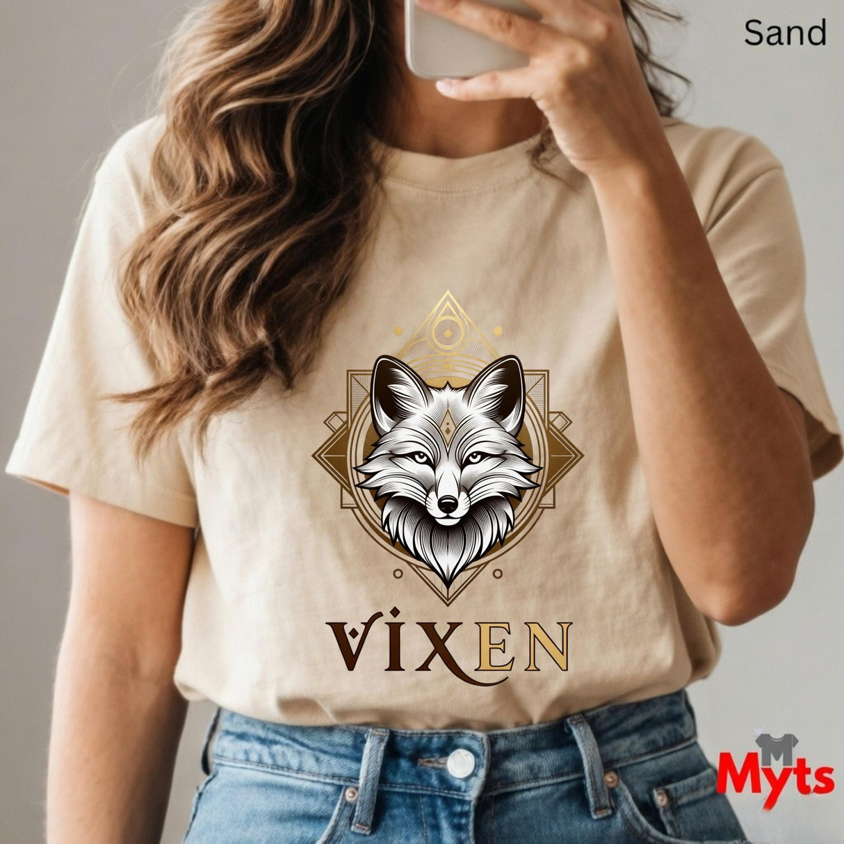 Person wearing a Sand  t-shirt with a fox graphic and 'VIXEN' text, holding a phone.