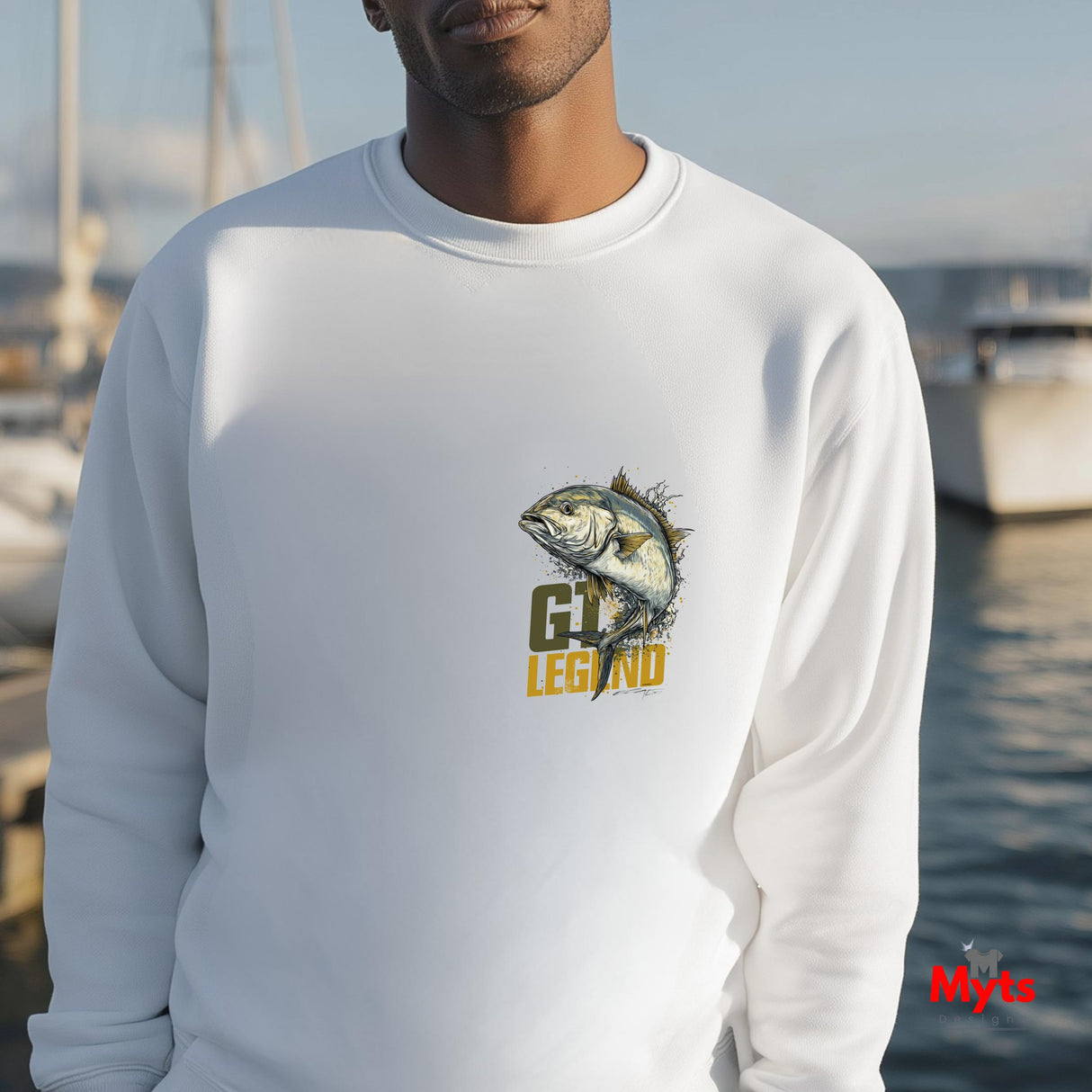 Person wearing a white sweatshirt with a fish graphic and 'MYTS' branding by a waterfront.