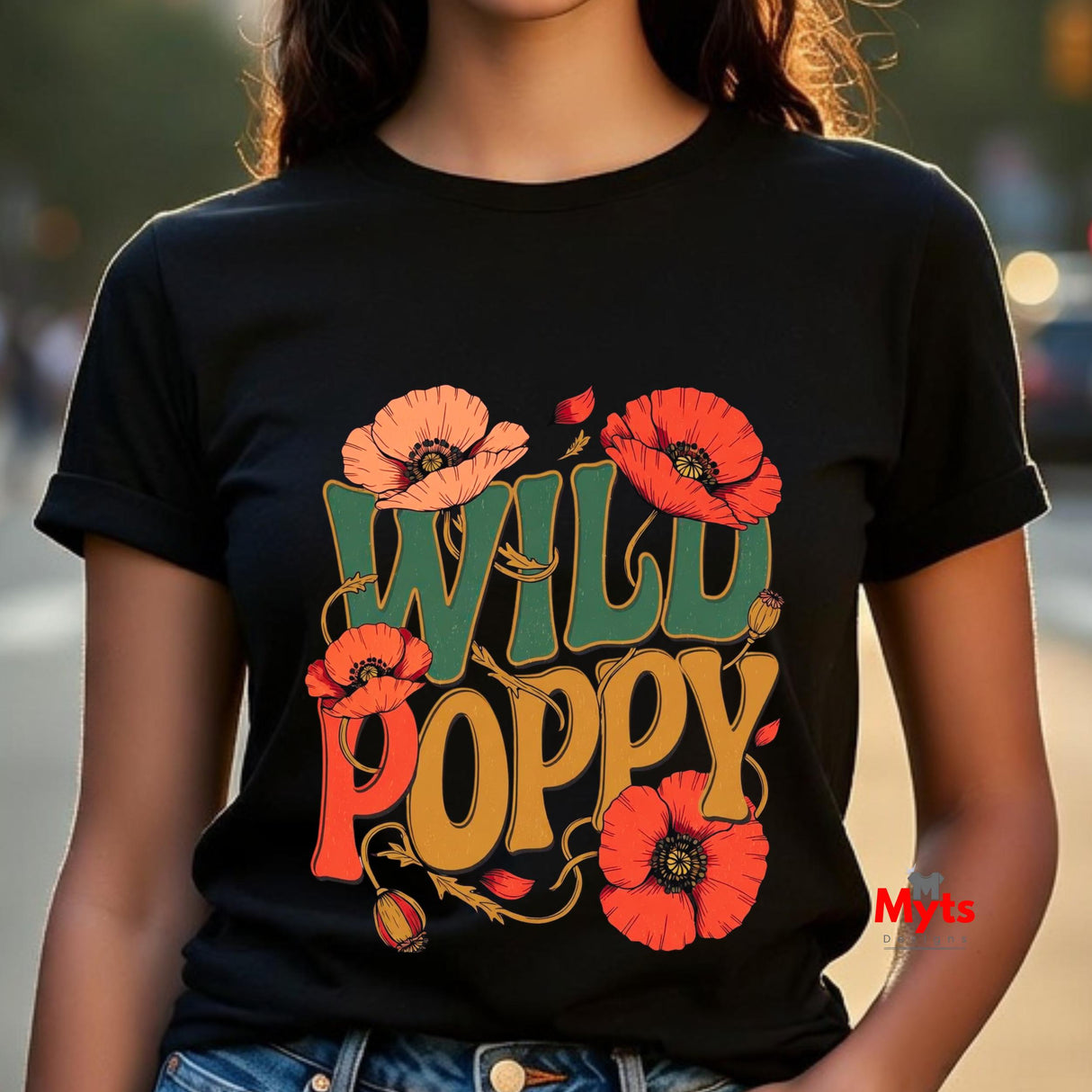 A person wearing a black short-sleeve T-shirt with a large retro-style graphic reading “WILD POPPY” in green, orange, and yellow, surrounded by red-orange poppy flowers. The photo is cropped from the neck to the hips, with a blurred outdoor street background.