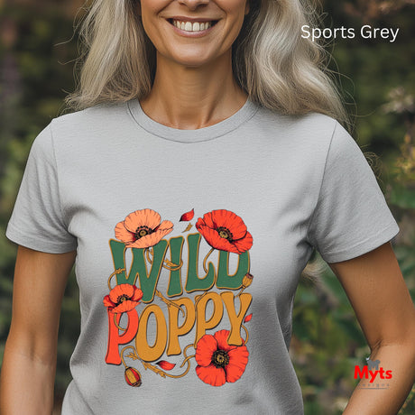 A woman wearing a light gray crewneck t-shirt with a colorful graphic that reads 'WILD POPPY' in green, orange, and red, surrounded by red poppy flowers. The background is a blurred green outdoor setting.