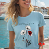 A woman wearing a light blue t-shirt with a 'Wild Poppy Spirit' graphic print featuring white and red poppies, set against a sunny outdoor waterfront background.