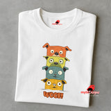 A folded white T-shirt featuring a quirky graphic of four stacked cartoon dogs in orange, yellow, teal, and golden tones with playful “WOOF!” text below the design.