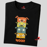 A folded black T-shirt featuring a quirky graphic of four stacked cartoon dogs in orange, yellow, teal, and golden tones with playful “WOOF!” text below the design.