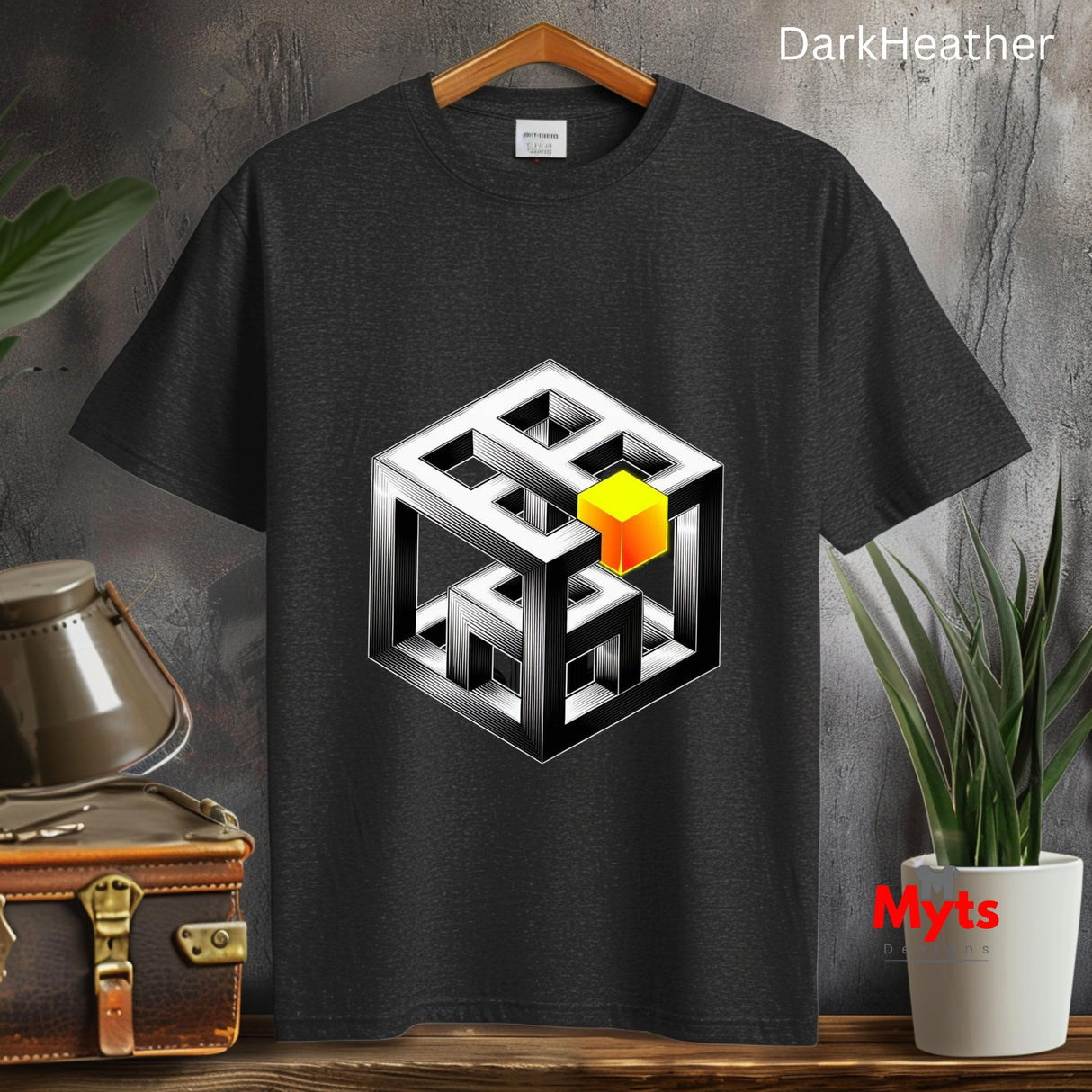 Dark Heather t-shirt with geometric design on a wooden surface with plants and a suitcase.
