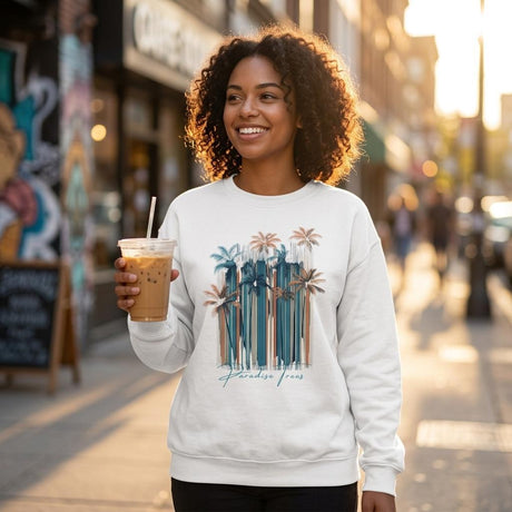 Woman wearing a sweatshirt with a palm tree design, holding an iced coffee, on a city street.