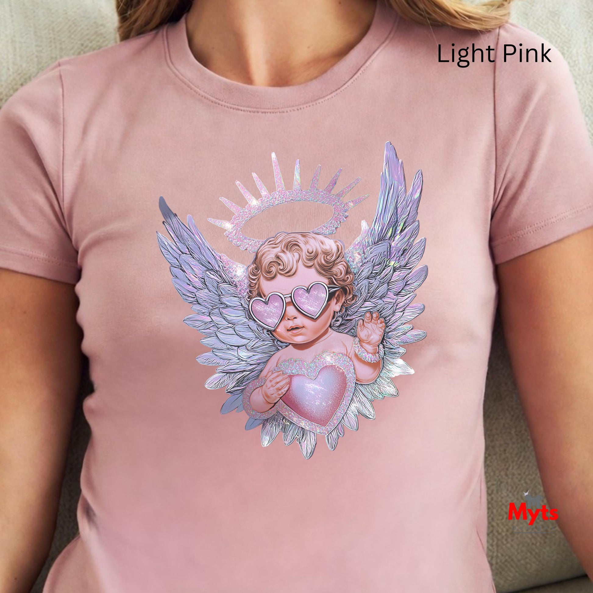 Light pink t-shirt with an angel design featuring wings and a heart, worn by a person.