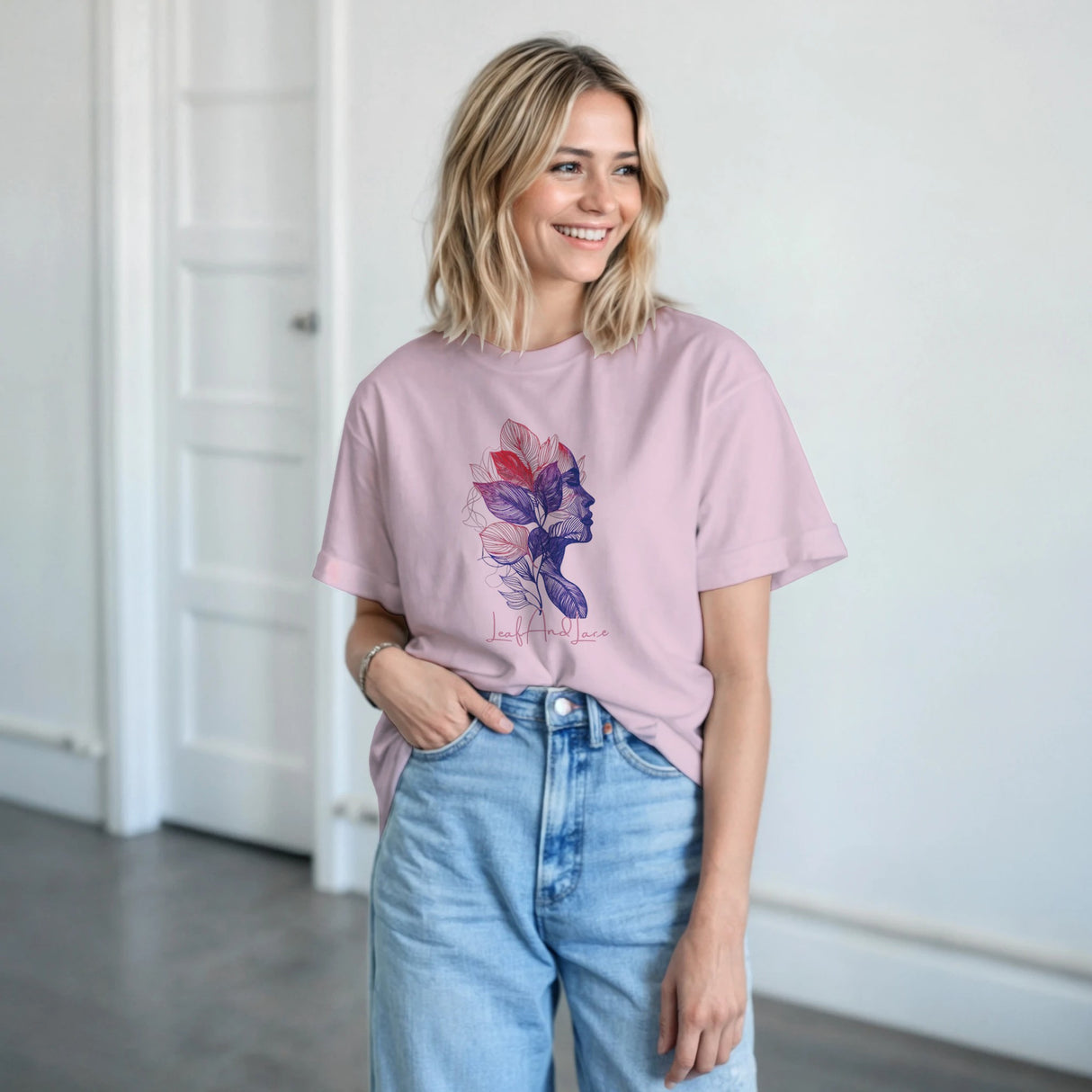 Woman wearing a pink t-shirt with a colorful design and light blue jeans indoors.