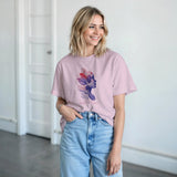 Woman wearing a pink t-shirt with a colorful design and light blue jeans indoors.