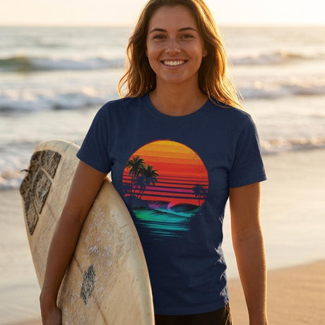 Woman holding a surfboard on a beach wearing a blue t-shirt with a colorful sunset design.