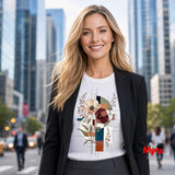 A woman stands on a city street wearing a white graphic T-shirt under a black blazer. The T-shirt features a colorful abstract floral design with cream, burgundy, teal, and brown elements.