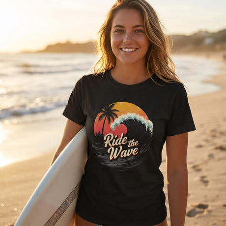 Woman on a beach holding a surfboard wearing a black t-shirt with a wave design and text.