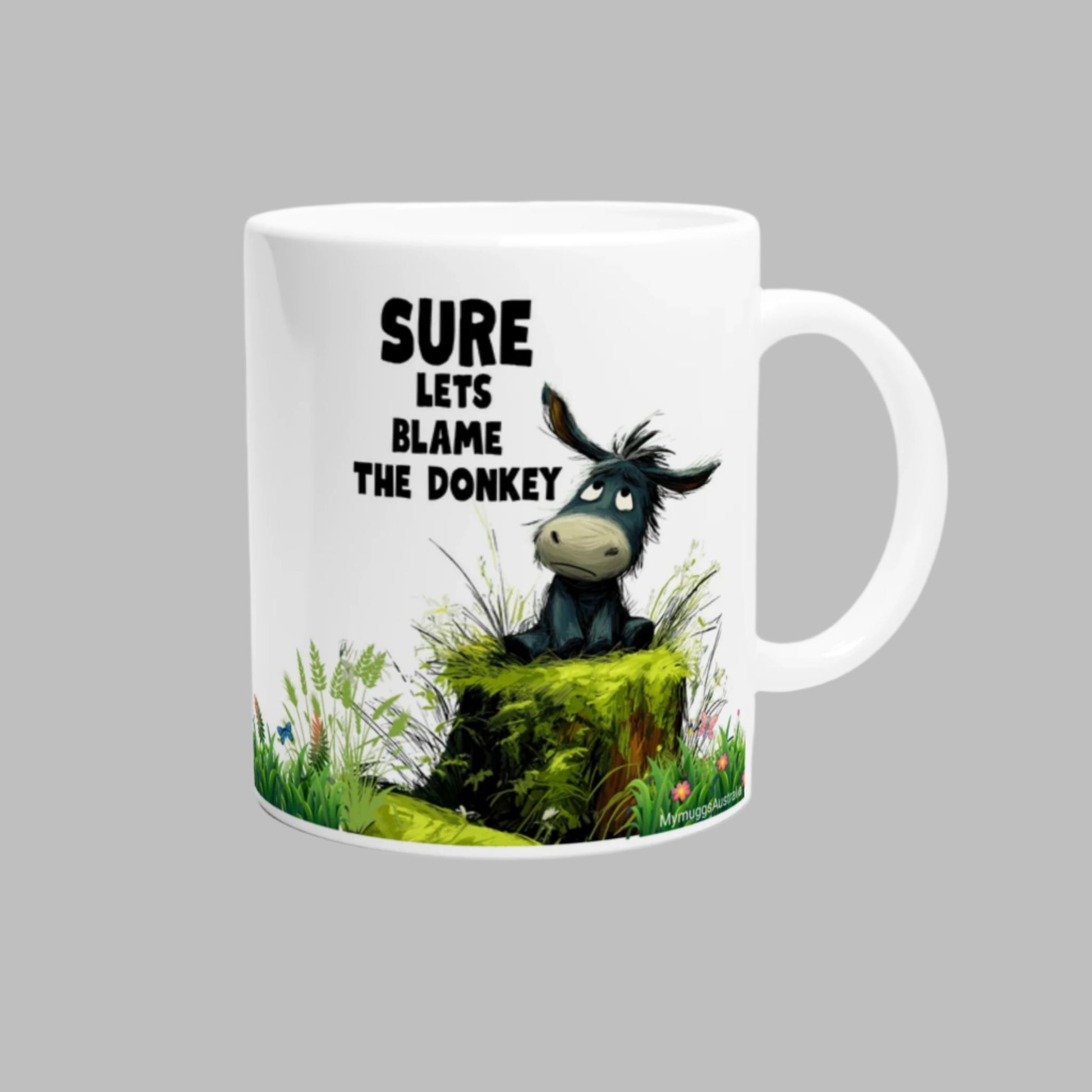 White ceramic coffee mug with a cute donkey sitting on a moss log, with the caption "Sure, Let's Blame The Donkey"