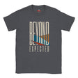 A dark heather gray t-shirt with a graphic print on the front that reads 'BEYOND EXPECTED' in cream lettering, featuring a stylized sunset design with blue, orange, and red geometric shapes.