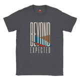 A dark heather gray t-shirt with a graphic print on the front that reads 'BEYOND EXPECTED' in cream lettering, featuring a stylized sunset design with blue, orange, and red geometric shapes.