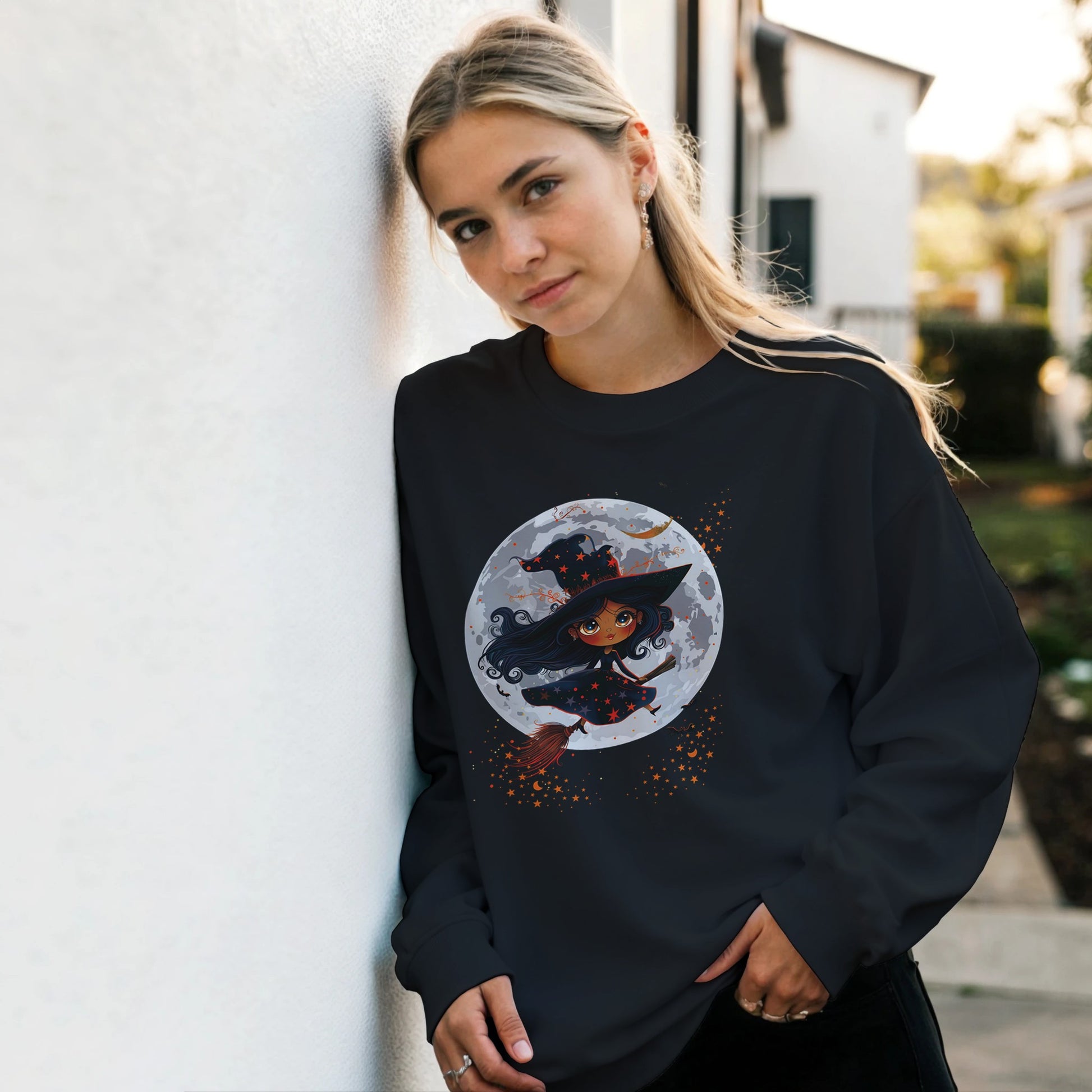 Woman wearing a black sweatshirt with a witch graphic design outdoors.