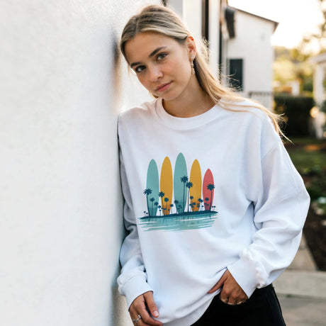 Woman wearing a white sweatshirt with colorful surfboard design outdoors.