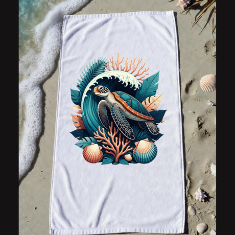 A white beach towel laid flat on sandy shore with ocean foam and seashells around it. The towel features a large colorful sea turtle illustration surrounded by coral, leaves, and shells.