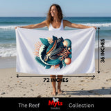 A woman on a beach holds up a large white towel or beach wrap featuring a colorful printed design of a fish, shell, and coral. Measurement arrows and text indicate the towel is 72 inches by 36 inches.