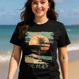 Front view of vintage beach T-shirt featuring palm trees and retro sunset graphic on black cotton tee worn by a woman waking on a beach