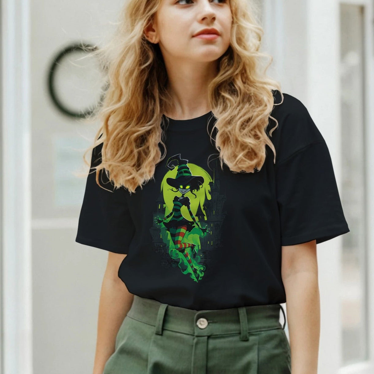 Woman wearing a black t-shirt with a graphic design and green pants in an indoor setting.