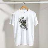 A white short-sleeve crewneck t-shirt hanging on a wooden hanger against a light gray wall. The shirt features a detailed graphic print of a koala sitting on a tree branch on the front.