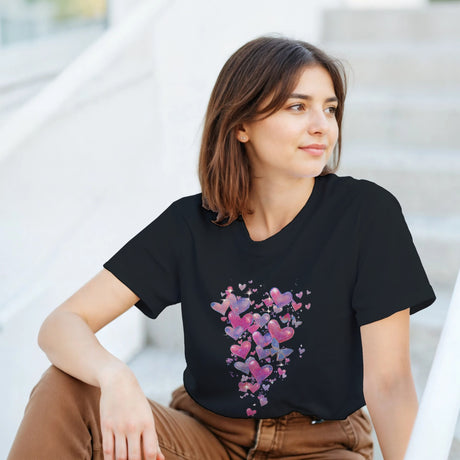 Woman wearing a black t-shirt with colorful heart design sitting outdoors.