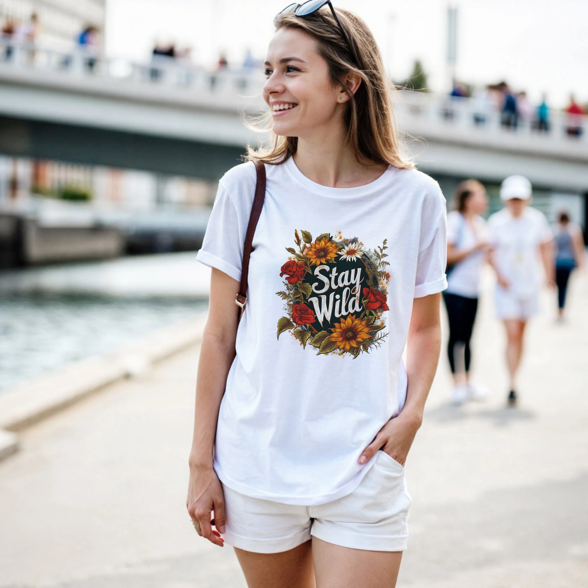 Woman wearing a white t-shirt with floral design and 'Stay Wild' text, standing outdoors.
