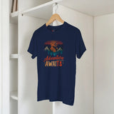 Navy blue t-shirt with 'Adventure Awaits' graphic on a hanger against a white wall.