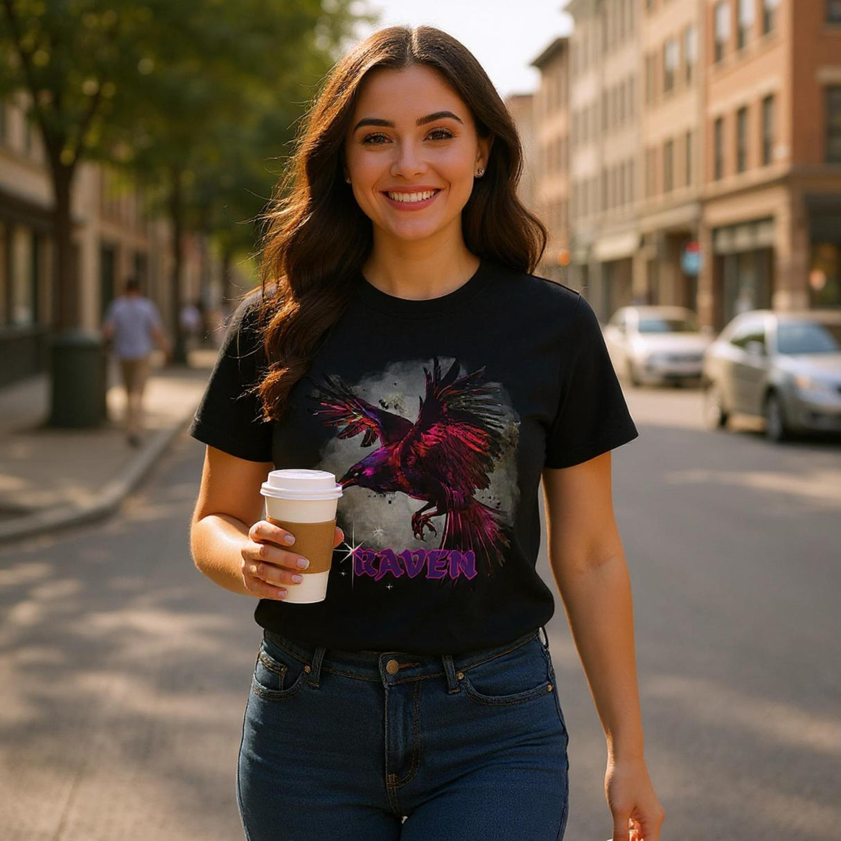 A woman walking on a city street holding a coffee cup, wearing a black t-shirt with a colorful graphic design.