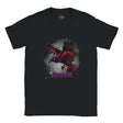 Black unisex T-shirt with a vivid magenta-and-black raven in flight against a smoky grey background and gothic purple “RAVEN” text, modeled outdoors by MytsDesigns.