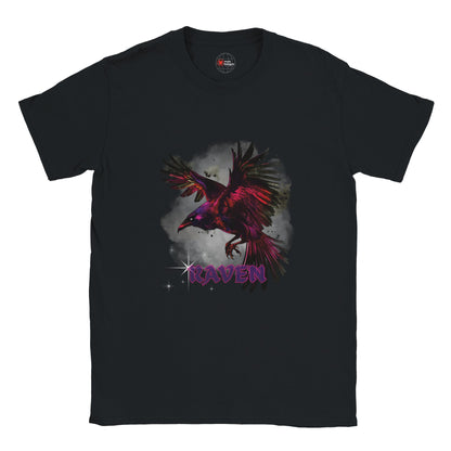 Black unisex T-shirt with a vivid magenta-and-black raven in flight against a smoky grey background and gothic purple “RAVEN” text, modeled outdoors by MytsDesigns.