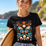 Smiling woman wearing a black dolphin butterfly graphic T-shirt while holding a surfboard at the beach.