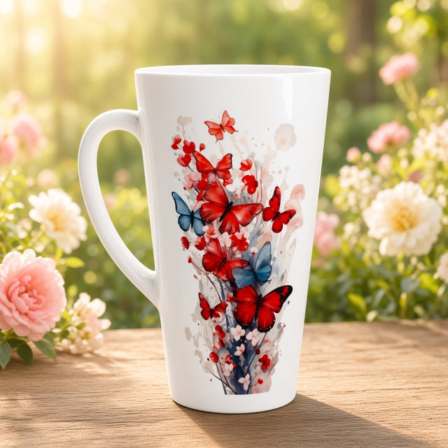 A tall white ceramic mug with a handle, decorated with a vibrant watercolor-style print of red and blue butterflies, placed on a wooden table with a blurred garden background of pink and white flowers.