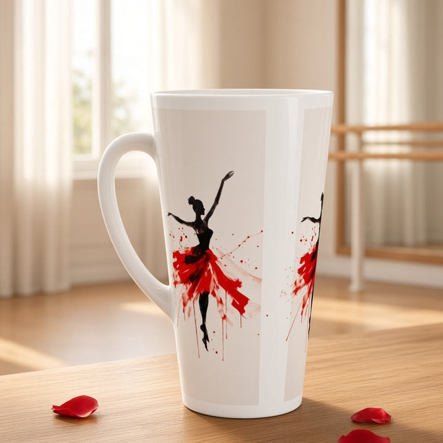 A tall white ceramic latte mug with a black and red ballerina silhouette print, set on a wooden table in a softly lit room with ballet barre in the background.