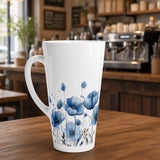 A tall white ceramic mug with a blue watercolor floral print, set on a wooden table in a blurred coffee shop background.