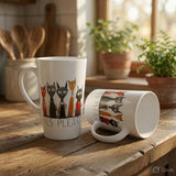 Two white ceramic mugs with a colorful cat illustration and the text 'YES PLEASE' are displayed on a rustic wooden table in a warm, sunlit kitchen setting.