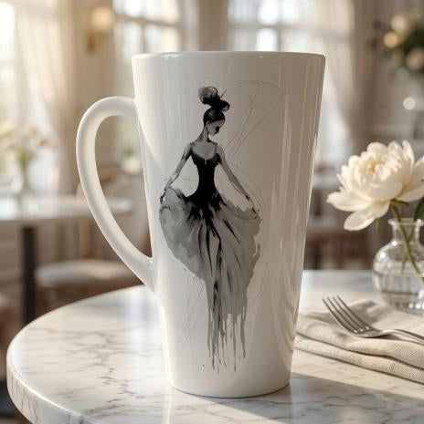 A tall white ceramic latte mug with a black and gray watercolor-style illustration of a ballerina, set on a marble table in a softly blurred cafe interior.