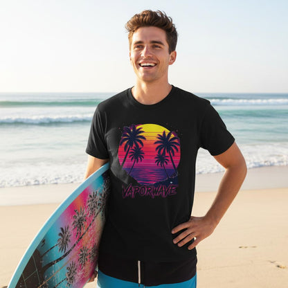 Man holding a surfboard on a beach wearing a black t-shirt with palm tree design