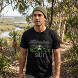 Man wearing a black t-shirt with a graphic design and 'SALTY' text, standing in a natural setting.