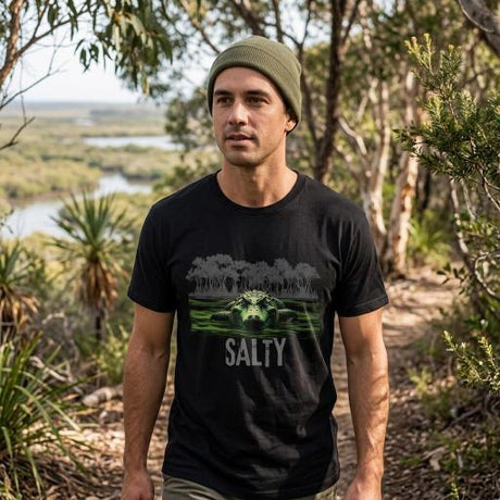 Man wearing a black t-shirt with a graphic design and 'SALTY' text, standing in a natural setting.