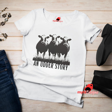 Flat lay view of white cotton T-shirt featuring illustrated cows and text “An Udder Story” – humorous farm-themed graphic tee

