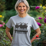 A woman wearing a sports grey cotton T-shirt featuring illustrated cows and text “An Udder Story” – humorous farm-themed graphic tee standing in a cottage garden

