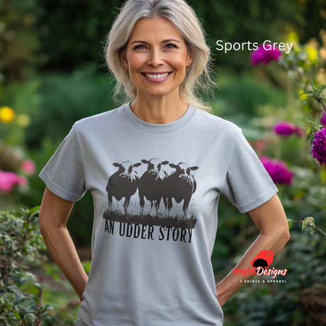 A woman wearing a sports grey cotton T-shirt featuring illustrated cows and text “An Udder Story” – humorous farm-themed graphic tee standing in a cottage garden


