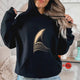 Black minimalist surf hoodie featuring elegant golden wave graphic worn in a cozy modern coastal lifestyle setting
