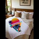 A white throw blanket with a colorful retro sunset and palm tree graphic is styled on a bed in a bedroom setting.