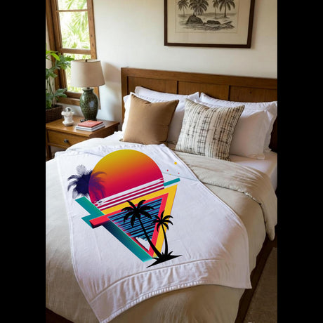 A white throw blanket with a colorful retro sunset and palm tree graphic is styled on a bed in a bedroom setting.